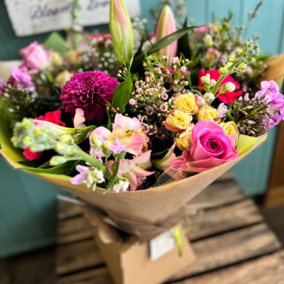 Bloom Boutique - A luxuriously full bouquet with a rich mix of pink roses, waxflower, dahlias, and spray roses in a bright, cheerful palette. Makes a bold gifting statement.